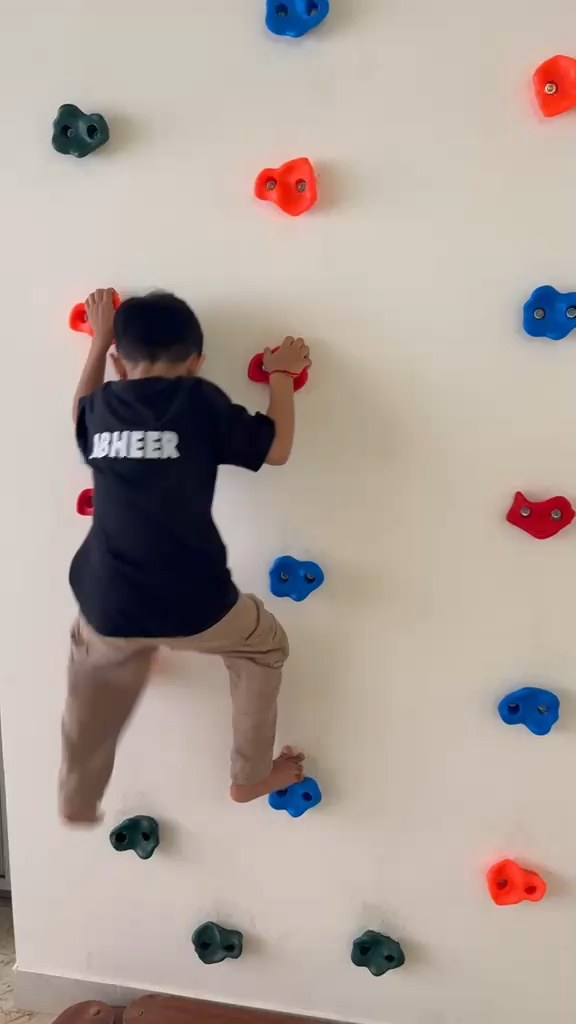 Child climbing the colorful rock wall at Vasishtha School